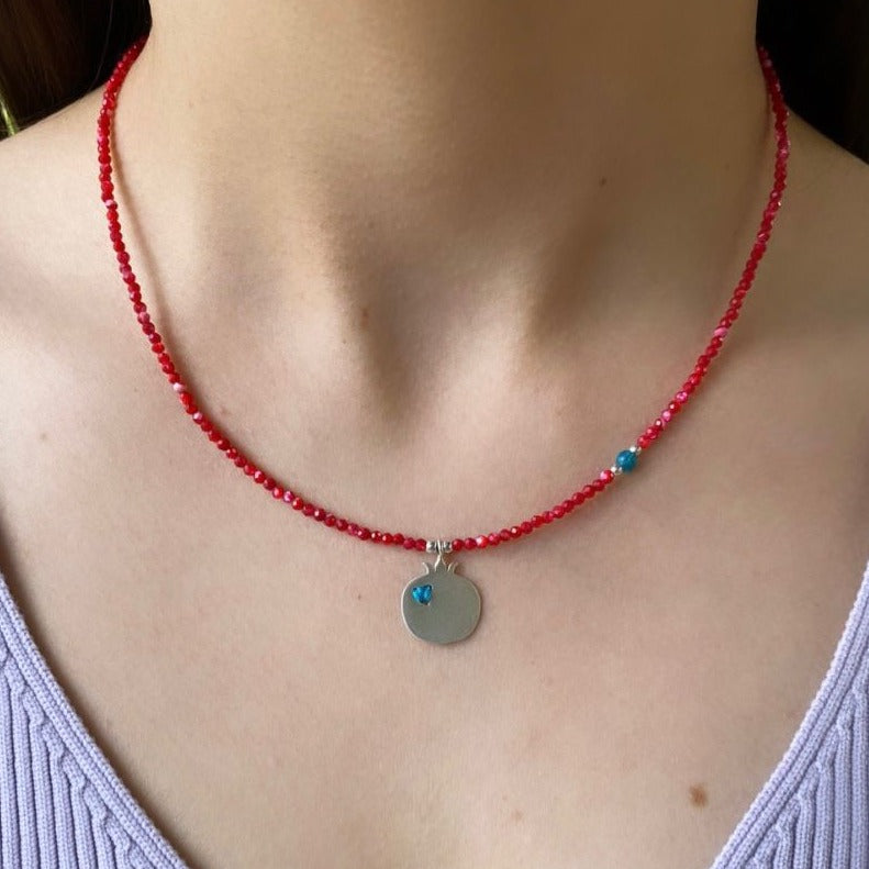 Pomegranate Silver and Coral Necklace with delicate red beads and a silver pendant displayed on a woman's neck.