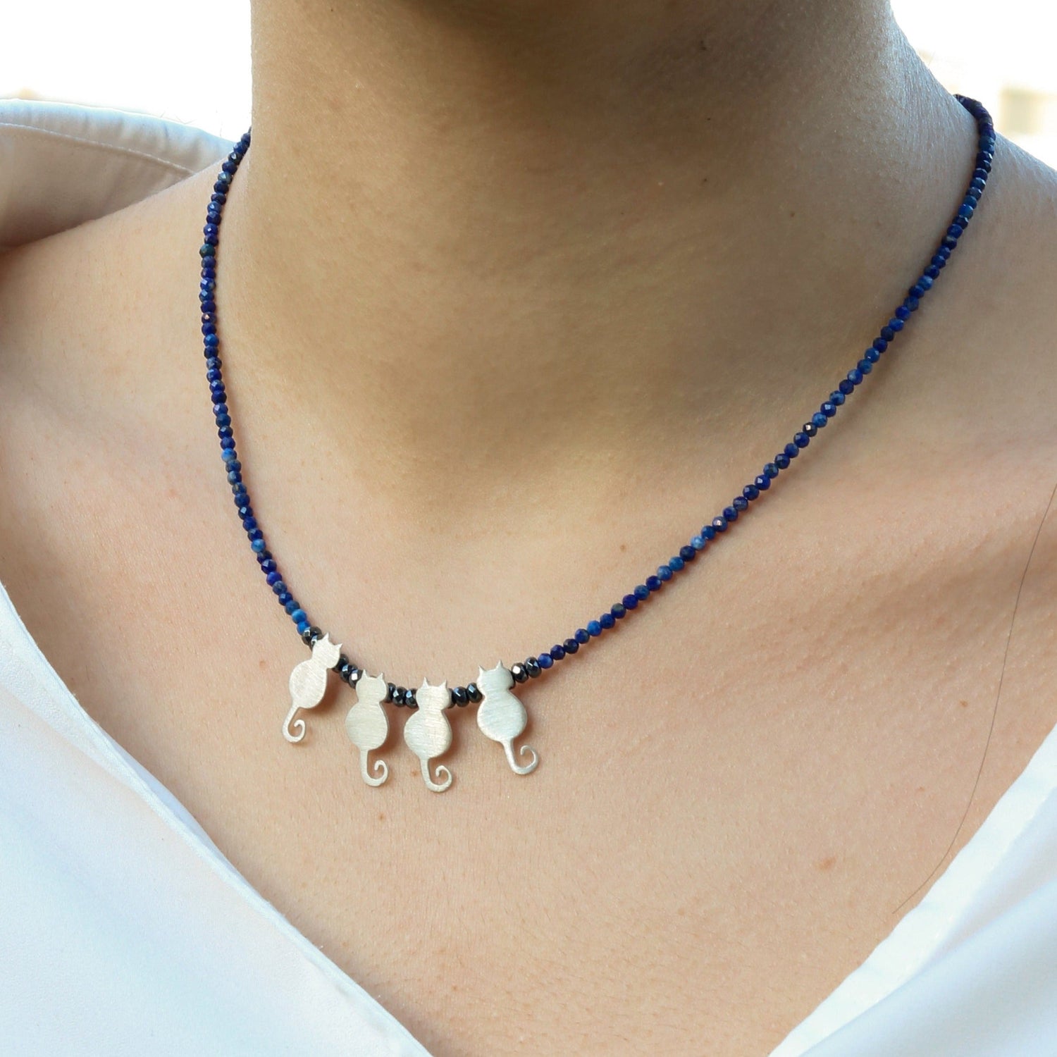 Close-up of Quartet Cats Lapis Silver Necklace featuring four silver cat charms on a lapis lazuli beaded chain, worn by a woman.