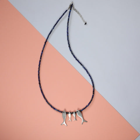 Quartet Fish Family Lapis Necklace against a pastel backdrop