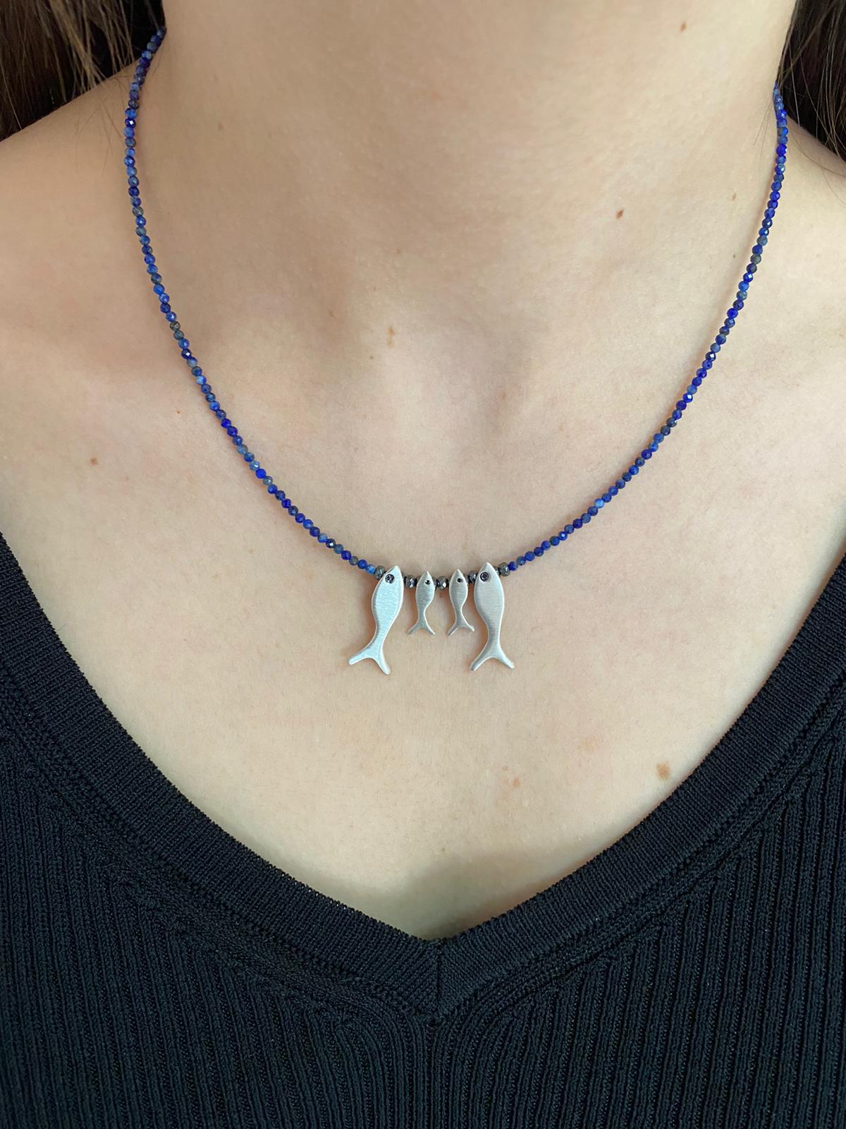 Close-up of a woman wearing a Quartet Fish Family Lapis Necklace with four fish pendants on a blue beaded chain