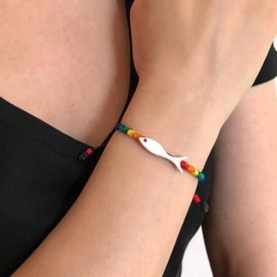 Close-up of woman wearing Rainbow Fish Silver Bracelet featuring colorful beads and a white fish charm.