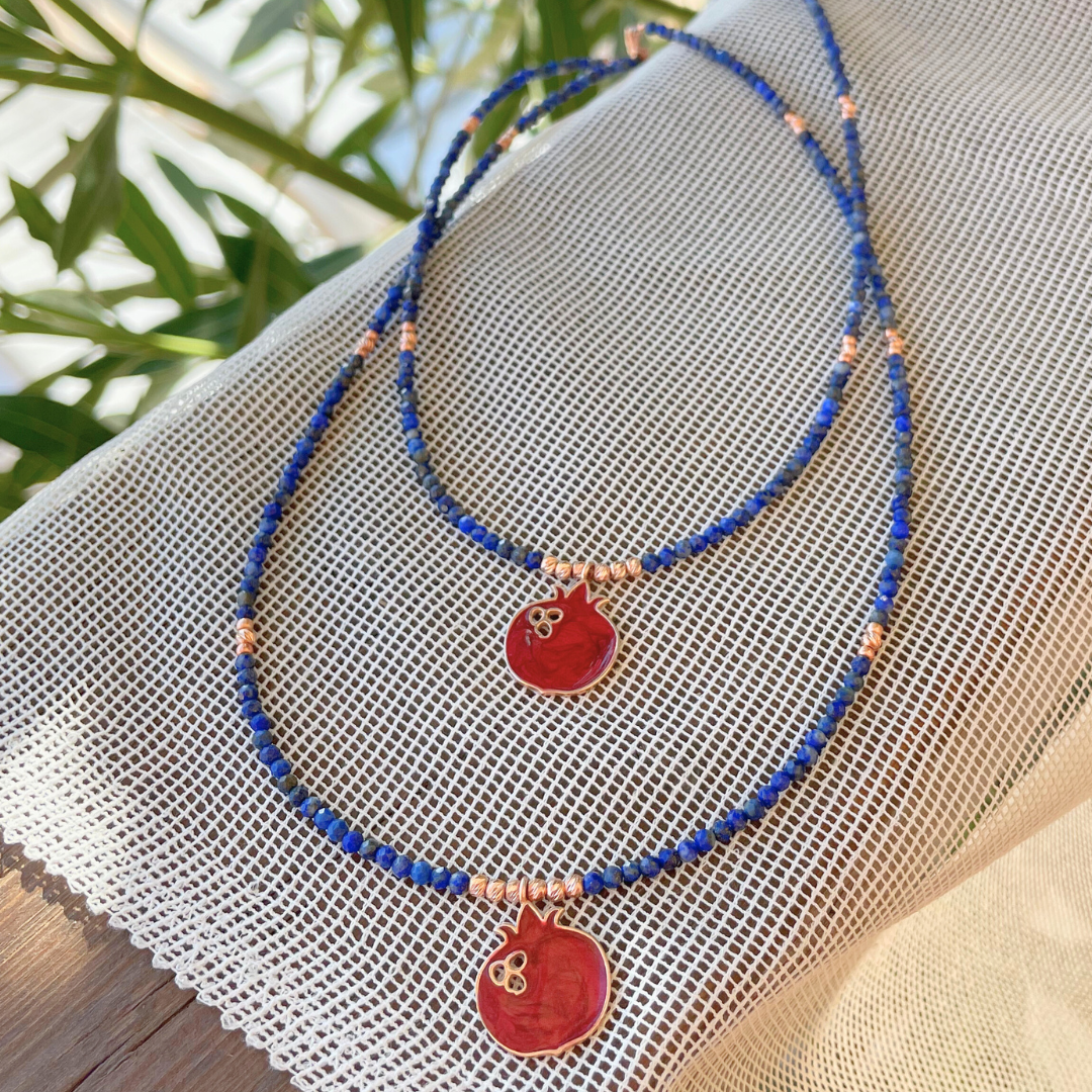 Elegant Red Pomegranate Lapis Necklace on a mesh fabric with green leaves in the background.