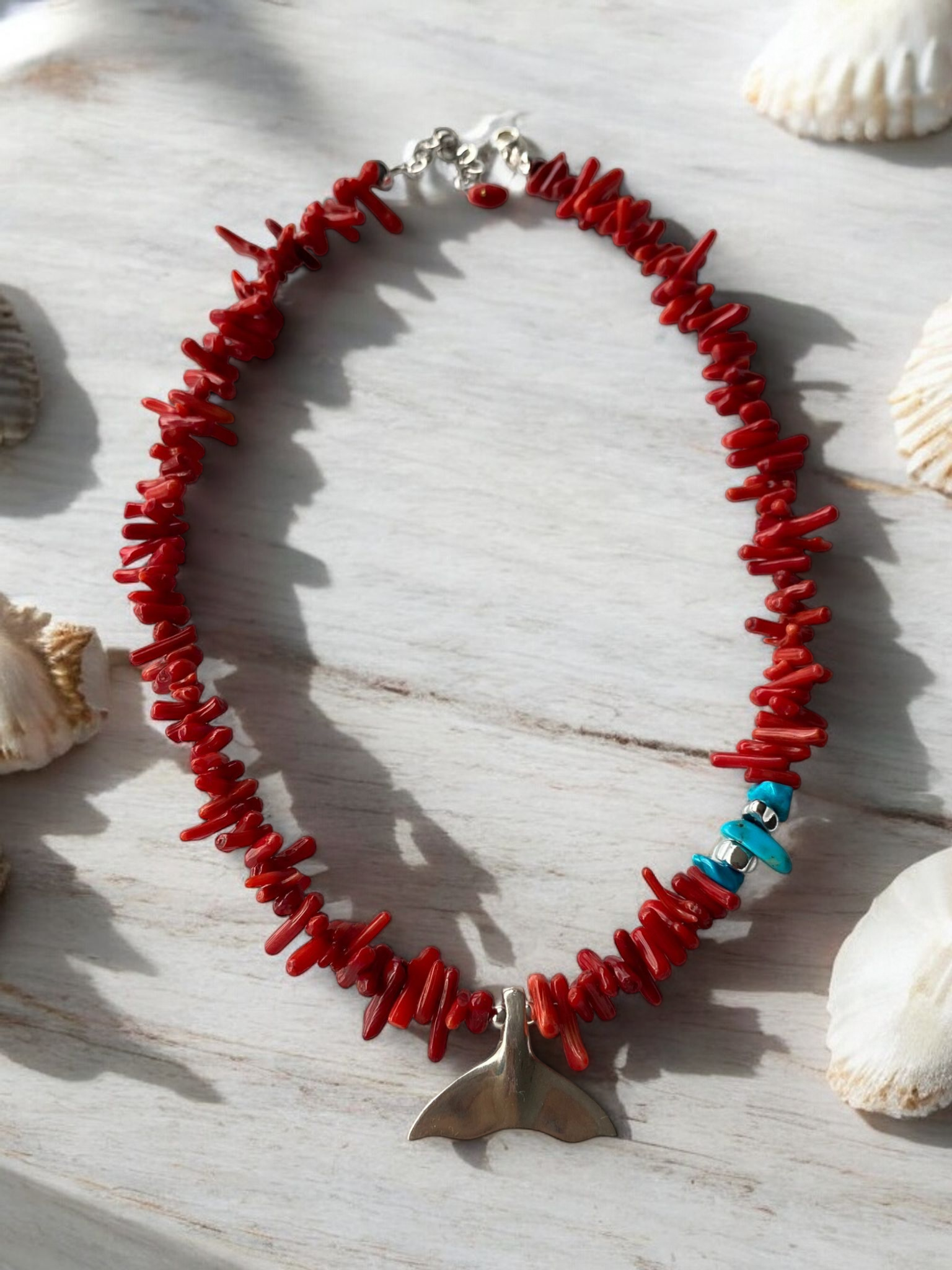 Reef Coral Gemstone Silver Fish Tail Necklace with vibrant red coral beads and a silver fish tail pendant among seashells.