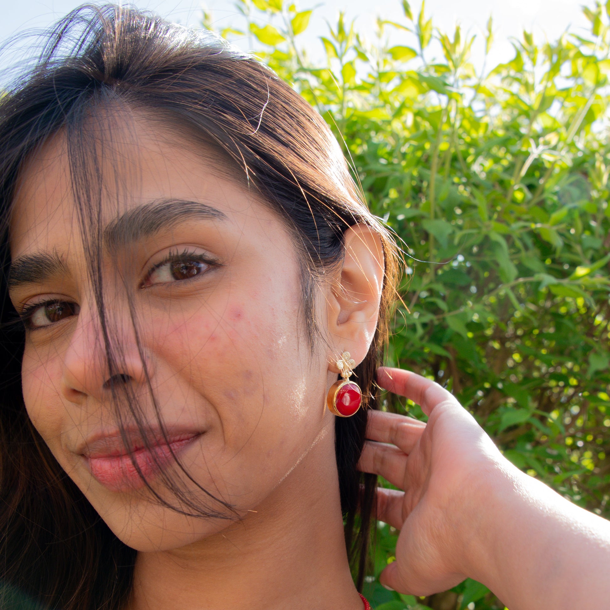 Woman wearing Rho Natural Coral Gemstone Earrings with greenery in the background