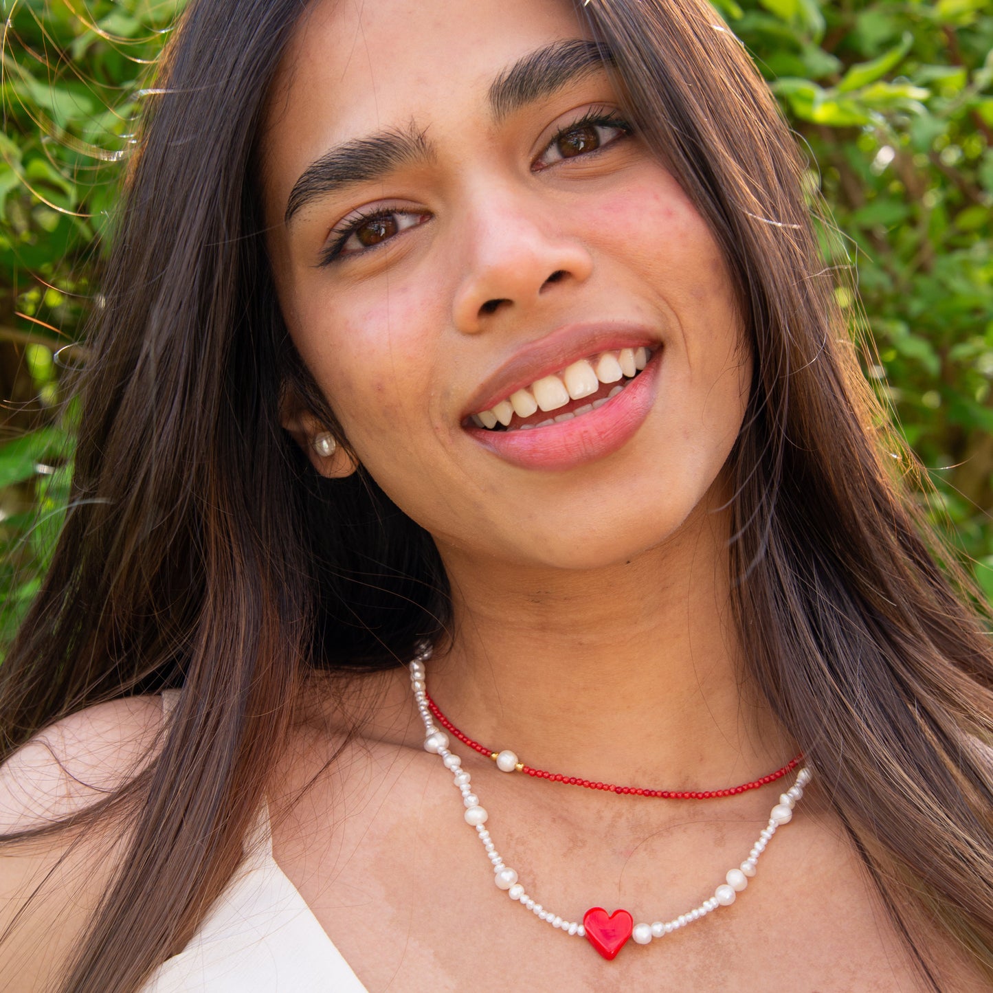 Rojo Natural Freshwater Pearl Necklace with Red Glass Heart Pendant worn by a smiling woman.