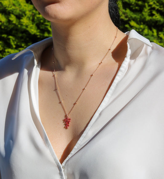 Rose gold plated silver chain with red coral pendant worn by a woman in a white shirt.