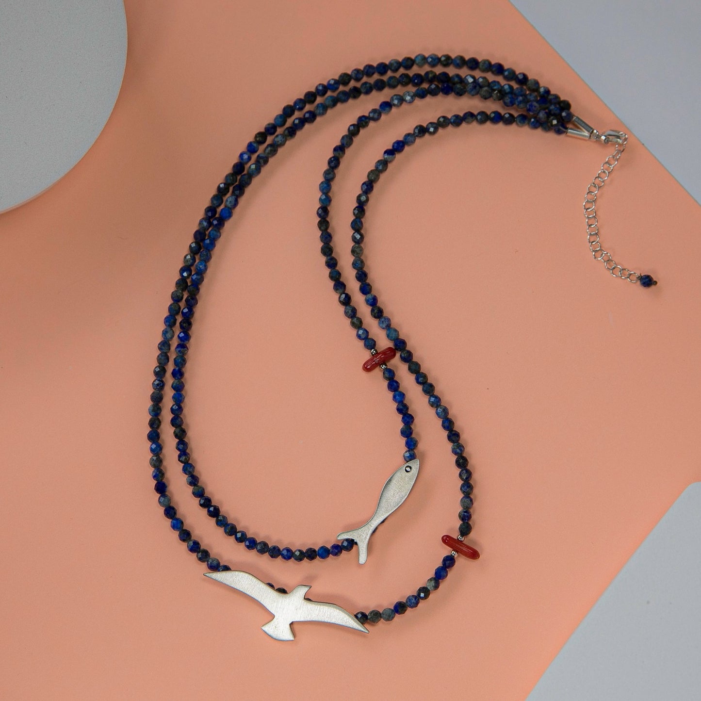 Seagull & Fish Lapis and Silver Necklace with lapis blue beads and silver bird and fish pendants on peach background.