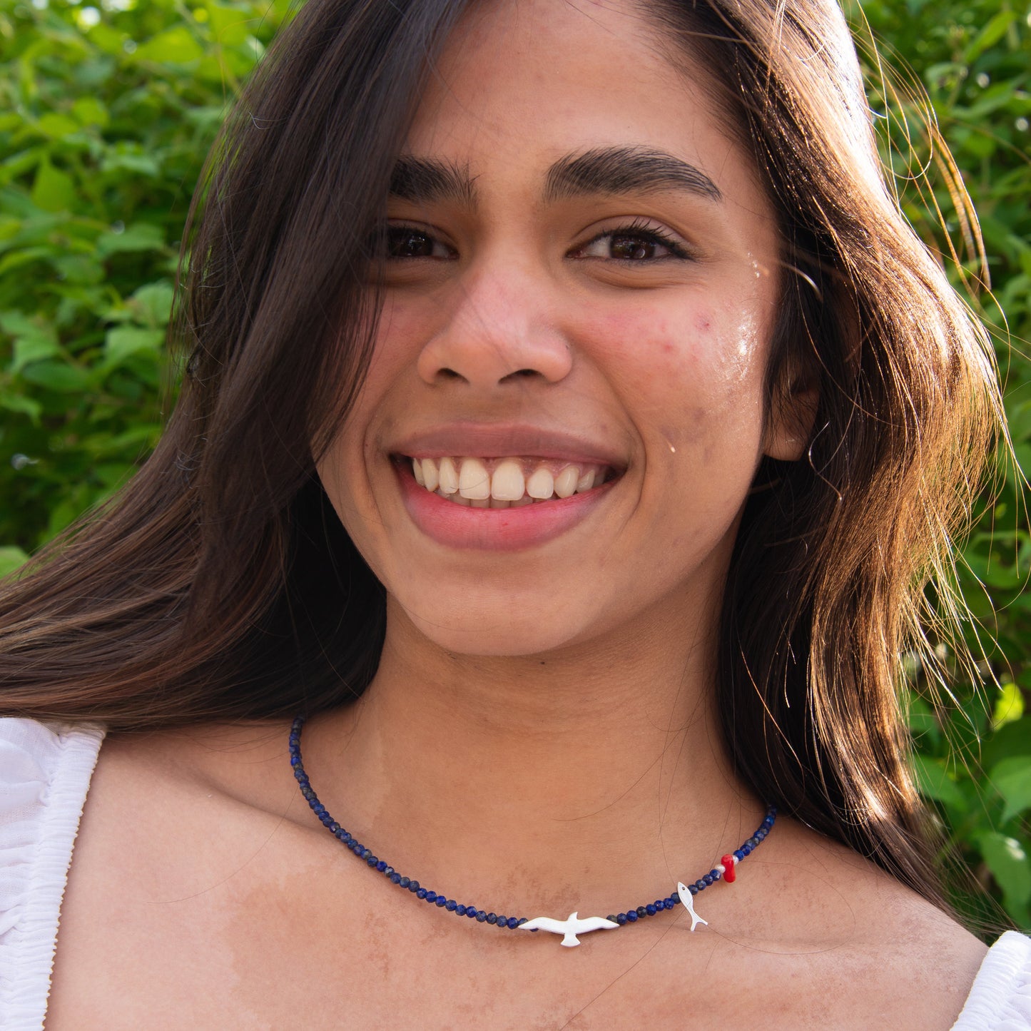 Woman wearing Seagull Lapis Lazuli Gemstone Necklace against a lush green background