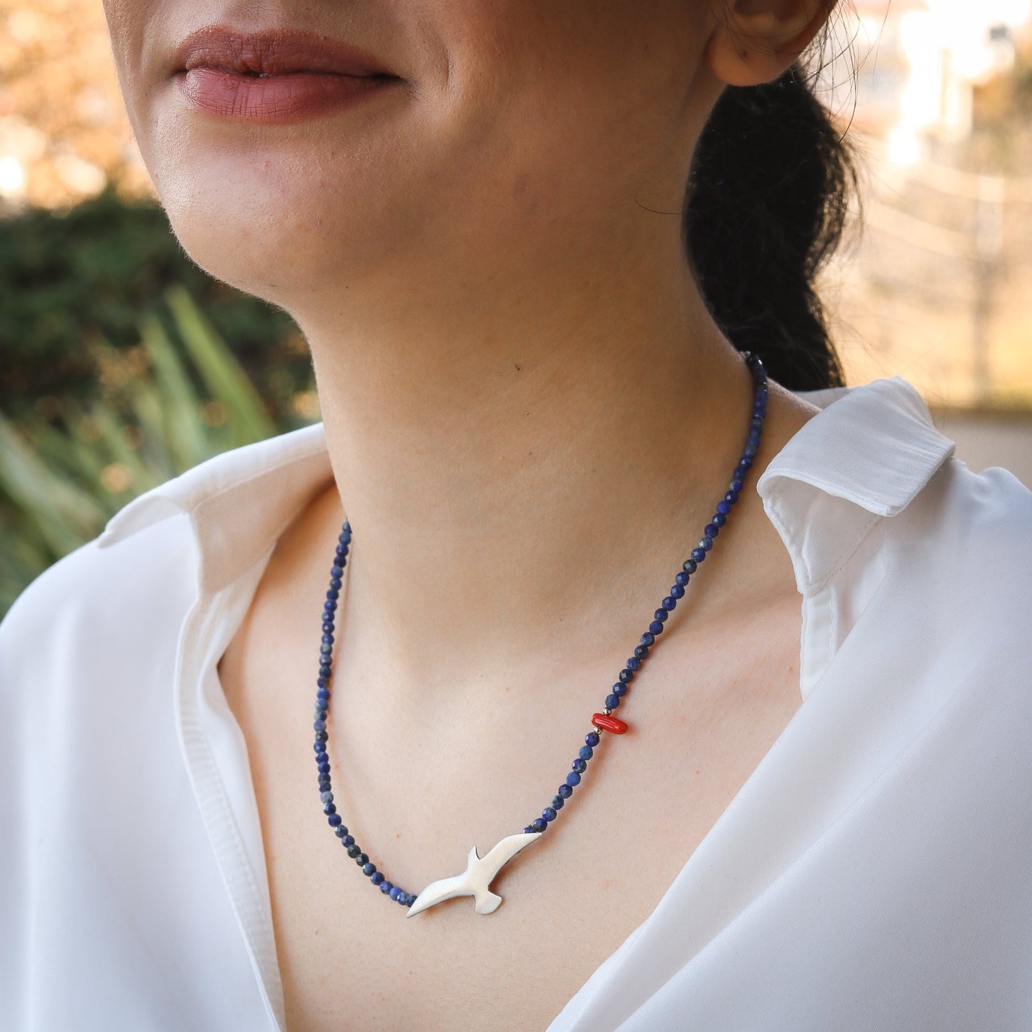 Woman wearing a Seagull Lapis Lazuli Gemstone Necklace with a white bird pendant and blue beads.