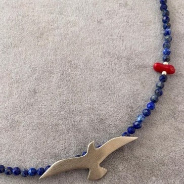 Seagull Lapis Lazuli Gemstone Necklace with a silver seagull pendant and blue beads on a grey background.