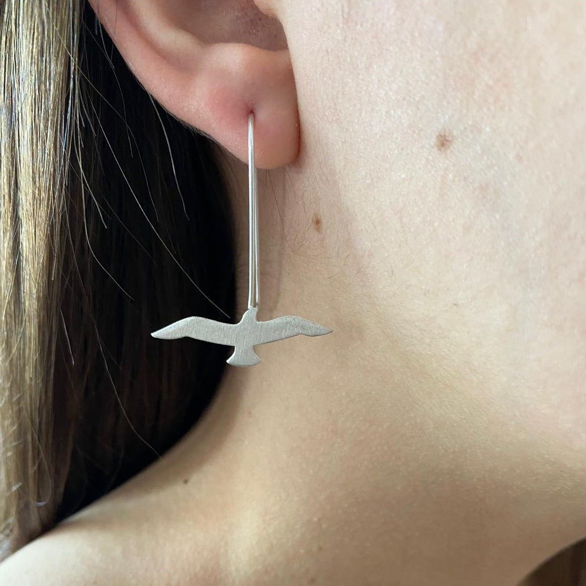 Elegant Seagull Silver Earrings suspended from a woman's ear, showcasing a minimalist bird design.