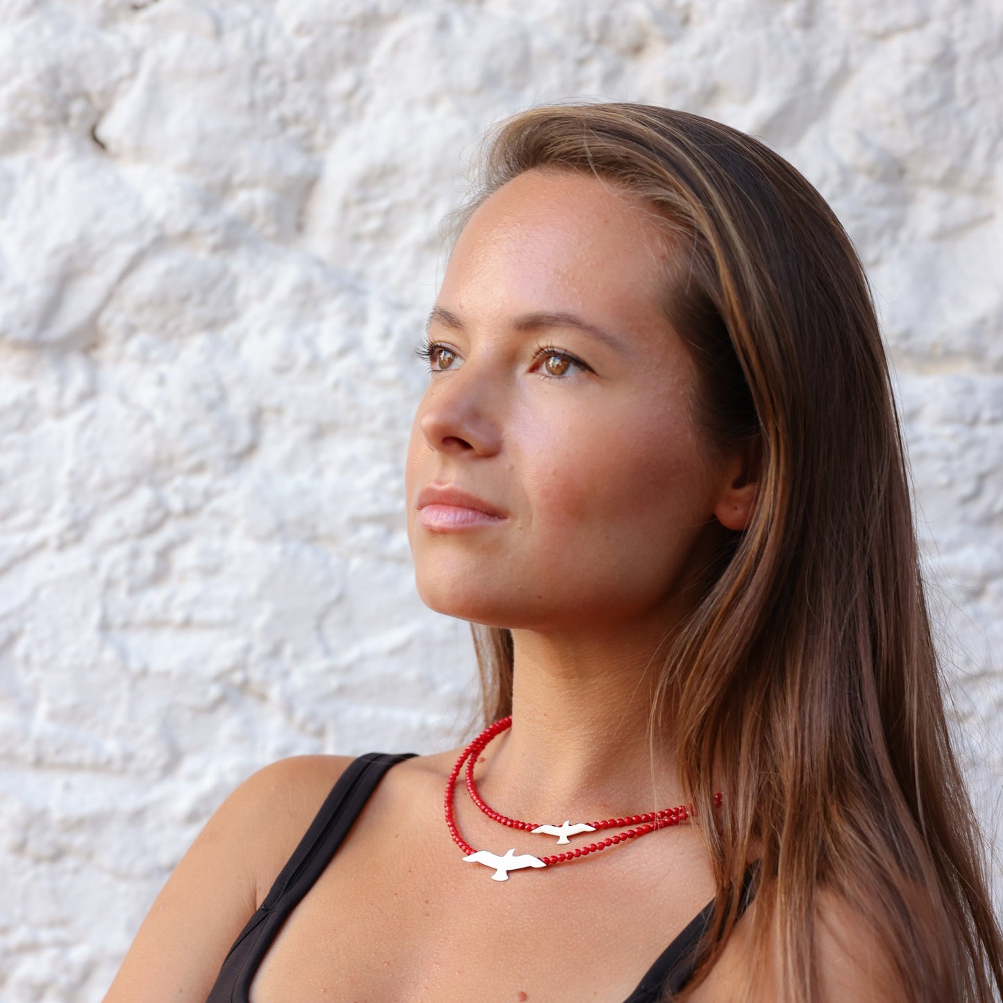 Woman wearing Seagulls Coral Silver Necklace with red beads and silver bird pendants against a white textured background.