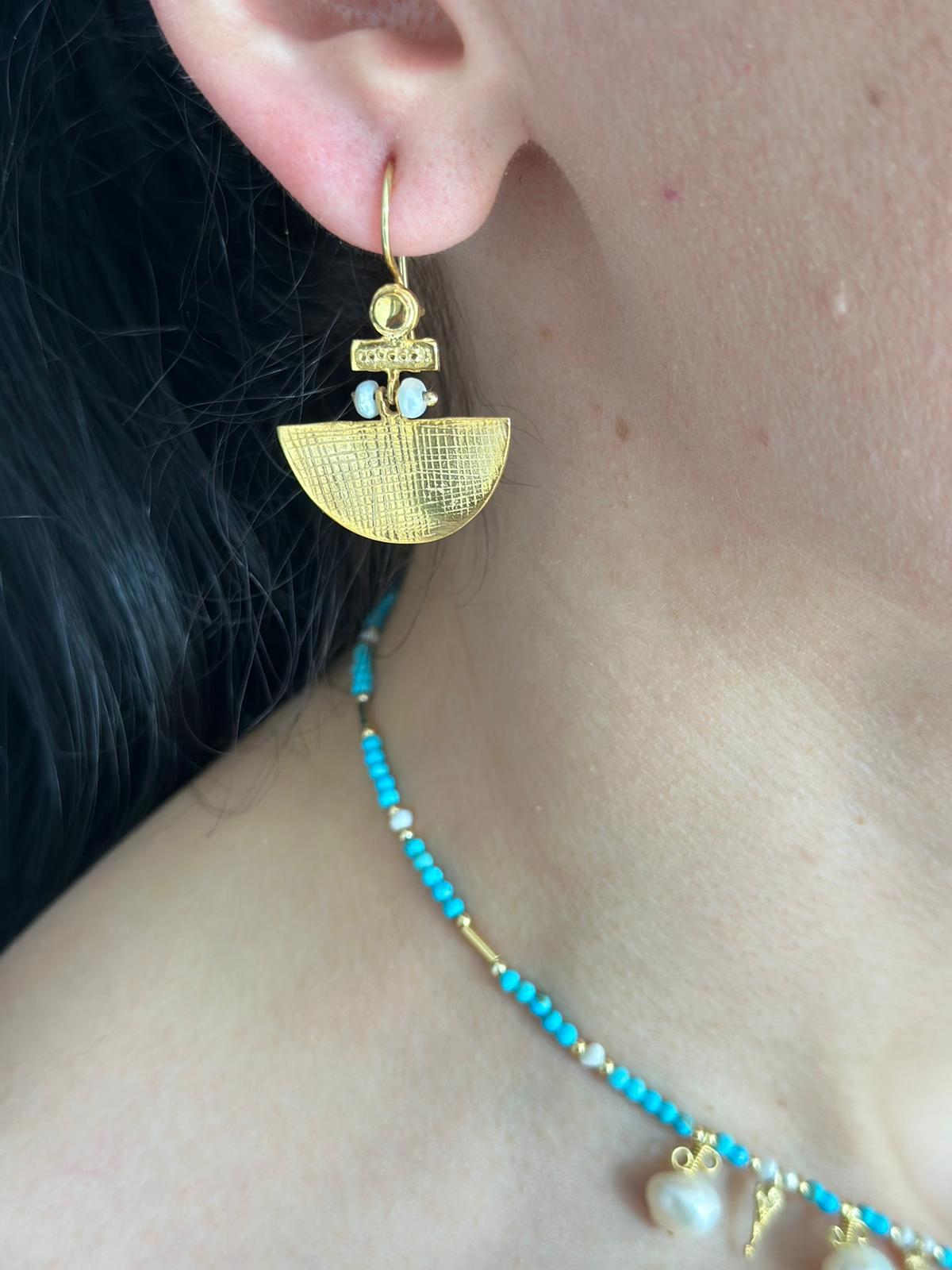 Close-up of a woman wearing Selena Silver Earrings - gold plated, featuring intricate design with a turquoise stone.