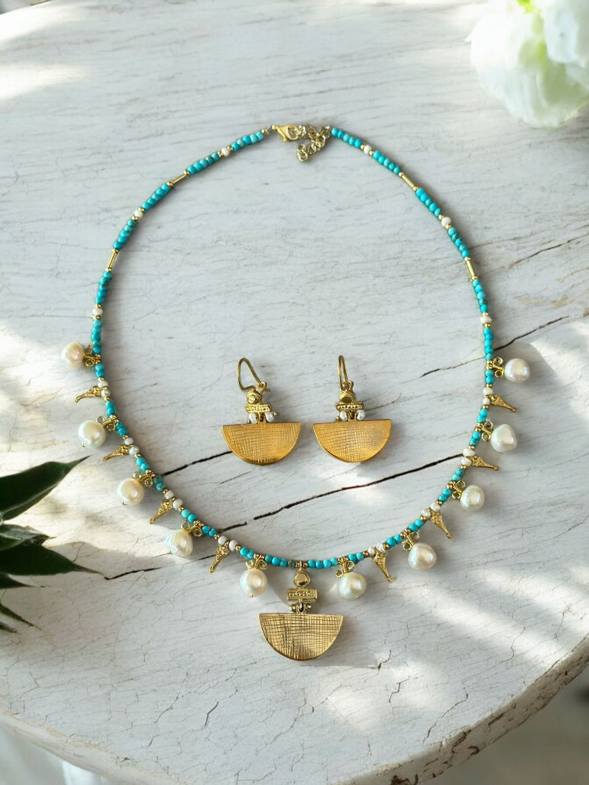 Selena Turquoise Necklace and Earrings Set - 14K Gold Plated with intricate gold accents and pearl detailing, displayed on a white rustic surface.