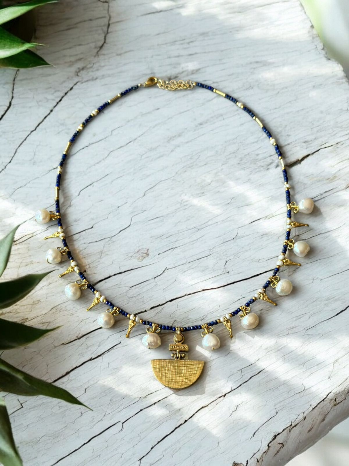 Selene Lapis Lazuli Gemstone and Pearl Necklace Gold Plated displayed on a white background with green plant accents