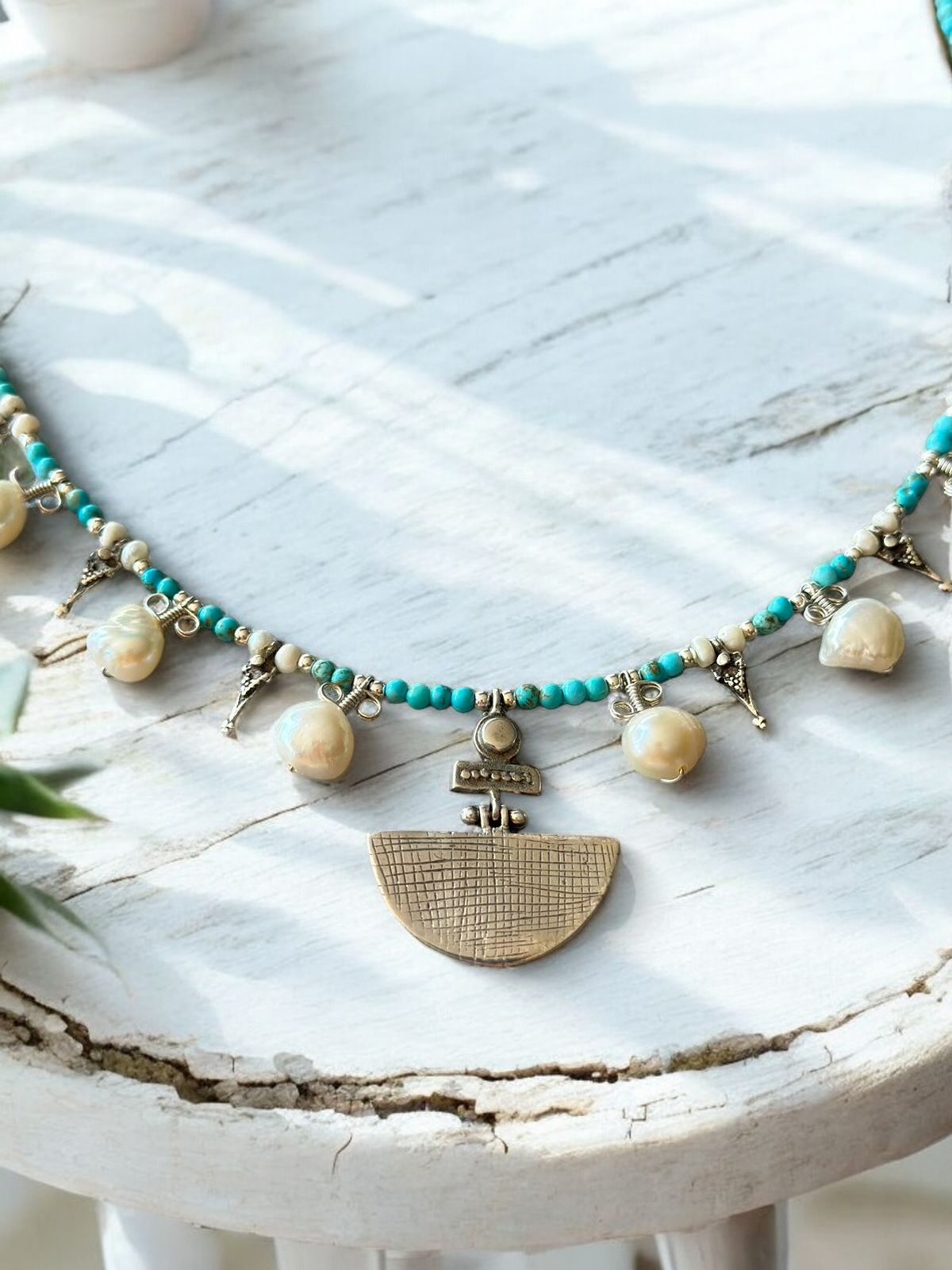 Selene Turquoise Gemstone and Pearl Necklace with intricate metallic pendant on a rustic white surface