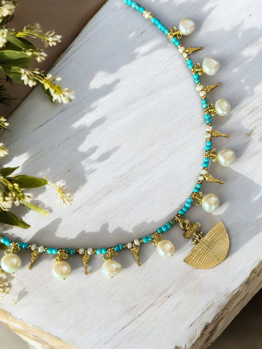 Selene Turquoise Gemstone and Pearl Necklace - Gold Plated with intricate design, laying on a wooden surface with flowers nearby.