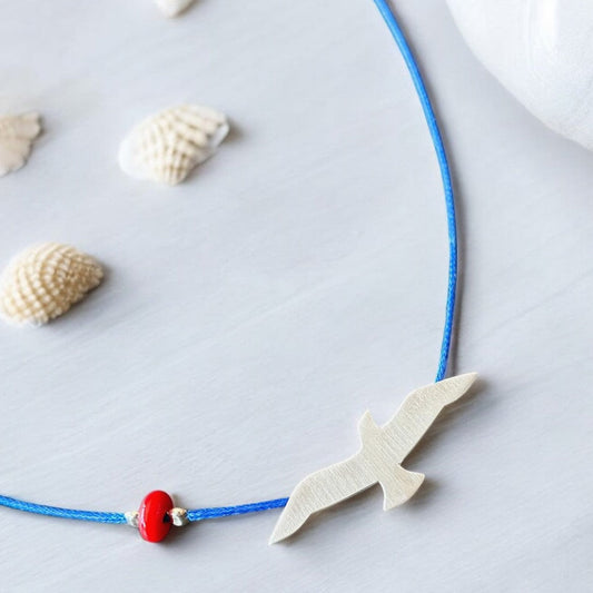 Elegant Silver Seagull Blue Cord Necklace with seashell accents featuring a white seagull-shaped pendant and a red bead