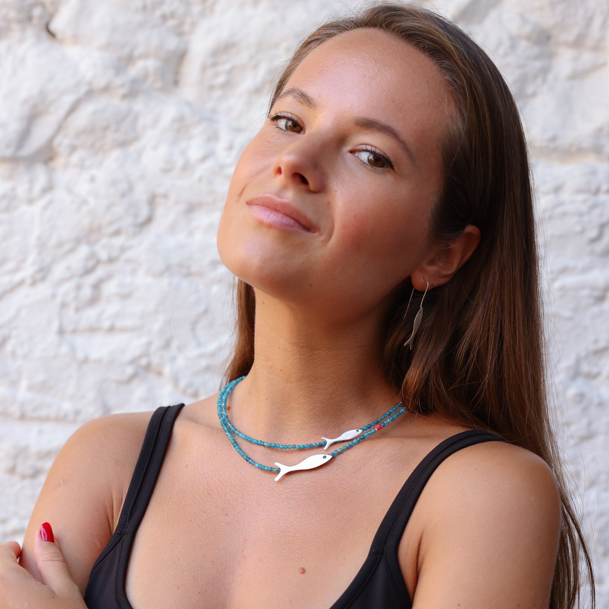 Woman wearing Small and Big Fish Apatite Silver Necklace, featuring blue beads and silver fish charms.