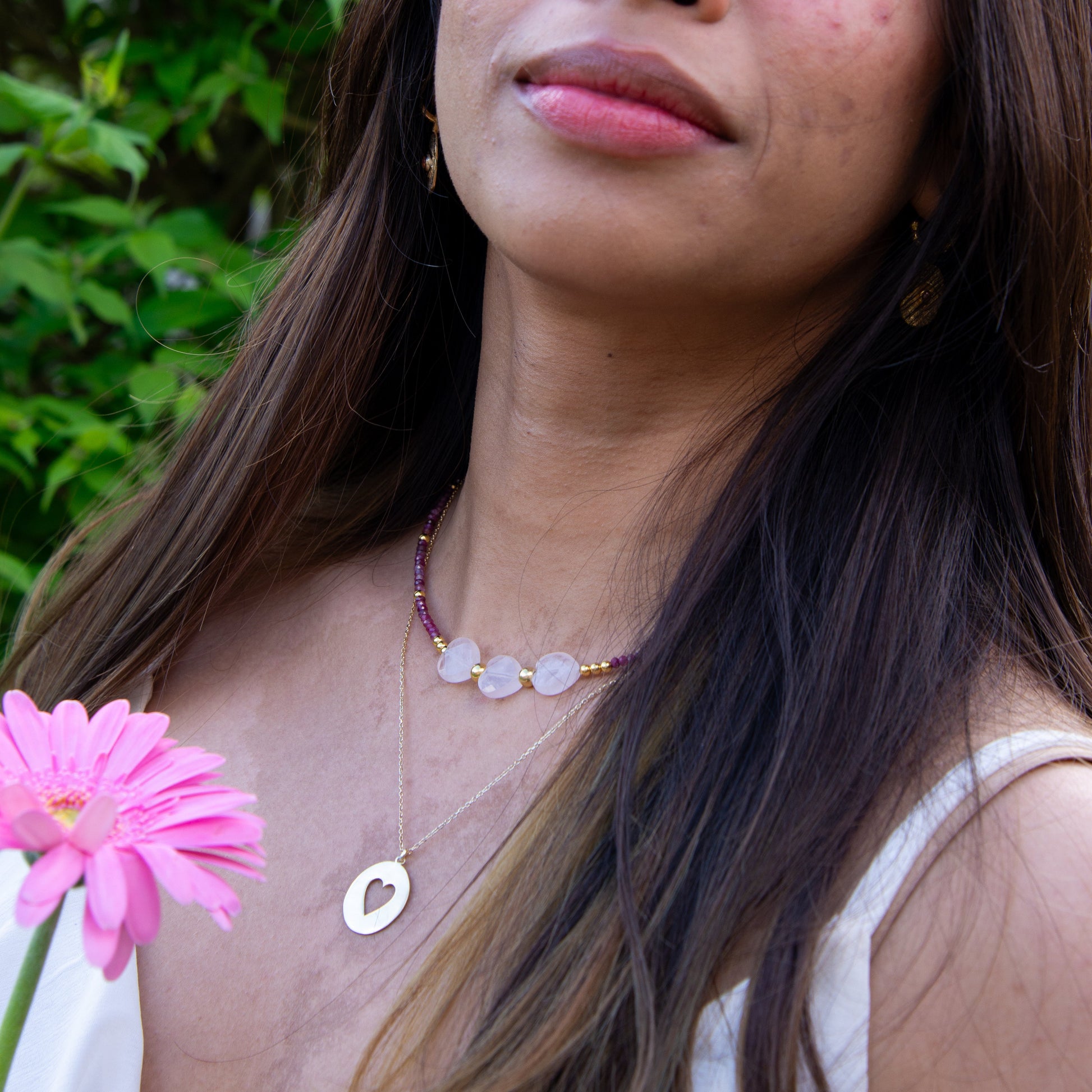 Woman wearing Three Hearts Tourmaline Gemstone Beaded Necklace, standing among greenery and holding a pink flower