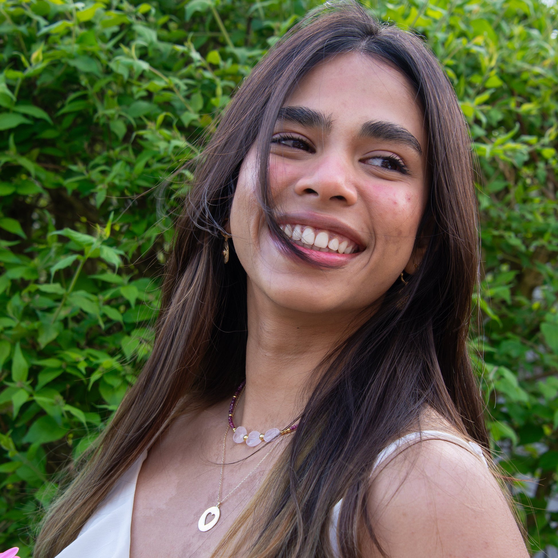 Woman wearing Three Hearts Tourmaline Gemstone Beaded Necklace, smiling in a lush green outdoor setting.