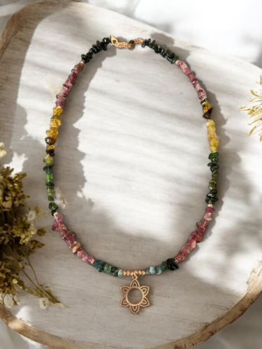 Tourmaline Flower Silver Necklace with colorful tourmaline stones and a flower pendant, displayed on a wooden tray with flowers around.