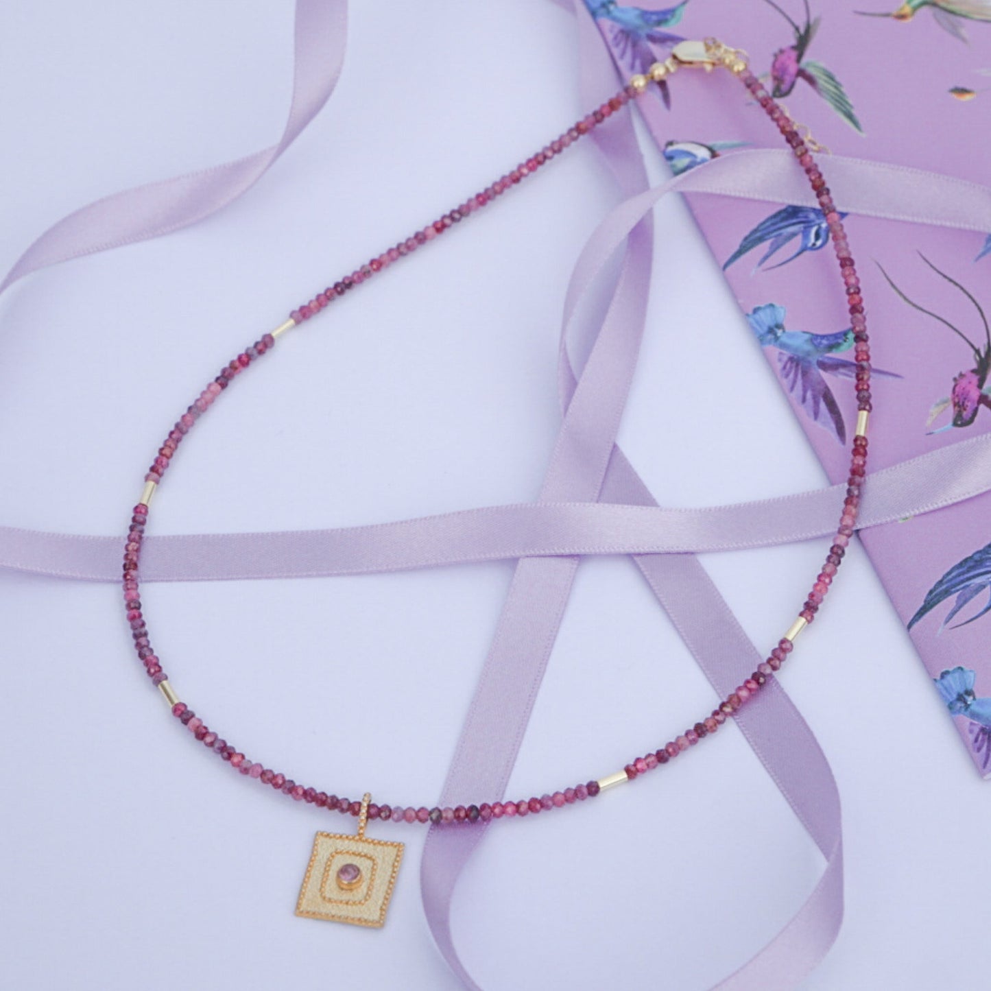 Tourmaline Gemstone Necklace with 14K Gold Plated 925 Sterling Silver Pendant on light purple ribbon and floral background.