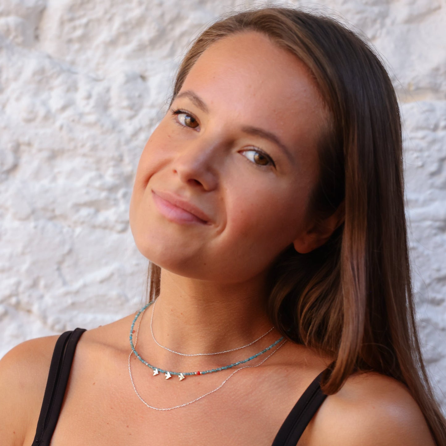 Woman wearing Trio Birdie Minimal Silver Necklace with colorful beads against a textured white background