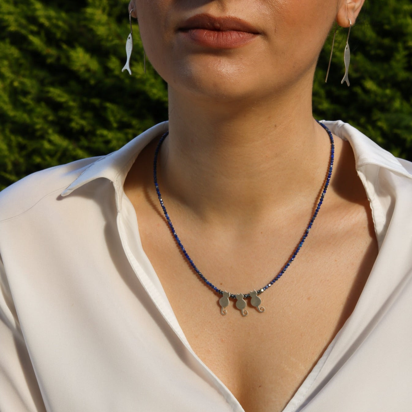 Woman wearing Trio Cats Lapis Silver Necklace with three cat pendants on a blue beaded chain.