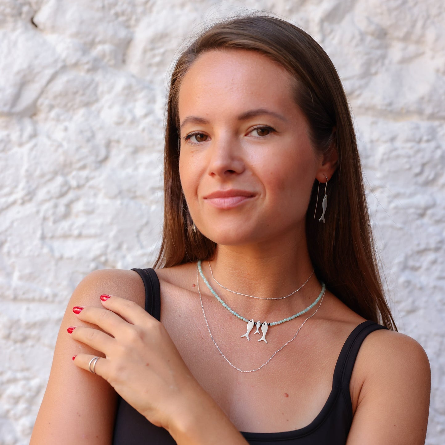 Woman wearing Trio Fish Family Amazonite Necklace with matching earrings against a white textured background.