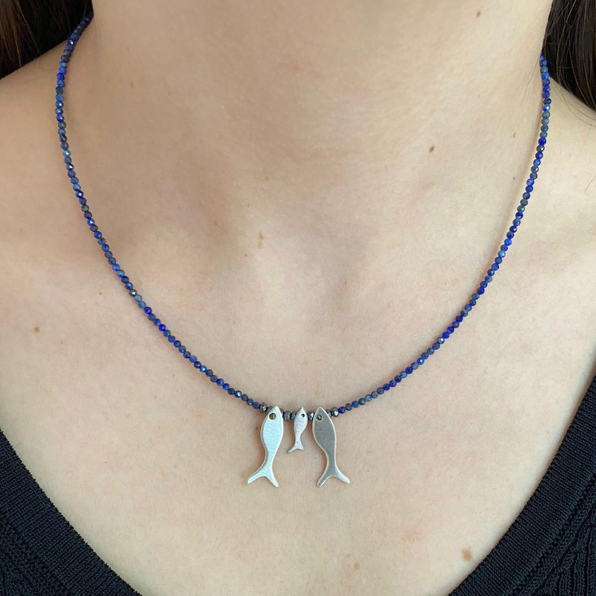 Trio Fish Family Lapis Necklace with three silver fish charms on a blue lapis bead chain worn by a person.