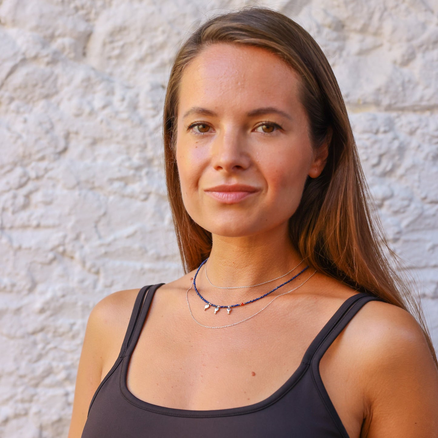 Woman wearing Trio Fish Minimal Silver Necklace against a textured white wall