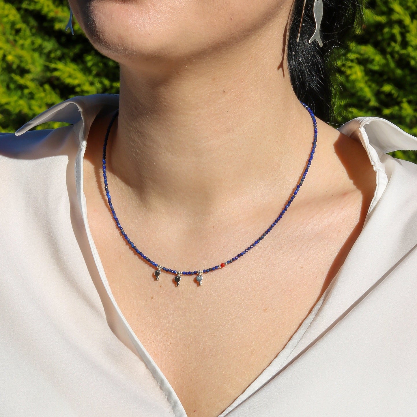 Woman wearing Trio Fish Minimal Silver Necklace with blue beads.