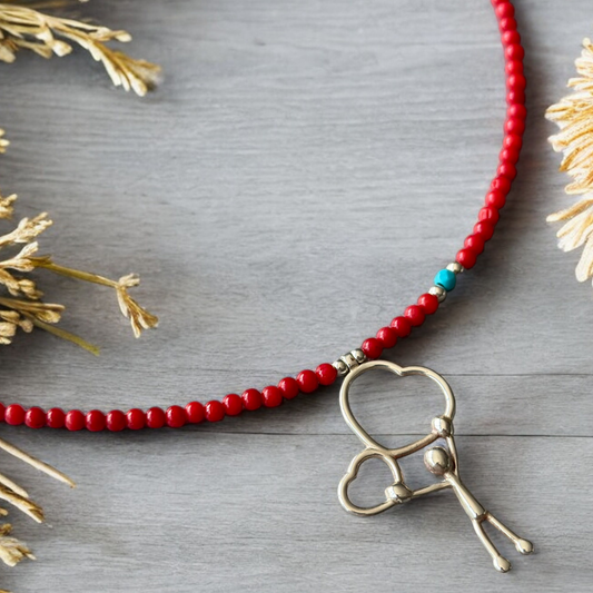 Two Hearts Coral Gemstone Necklace featuring red beads, a turquoise accent, and a silver heart pendant.